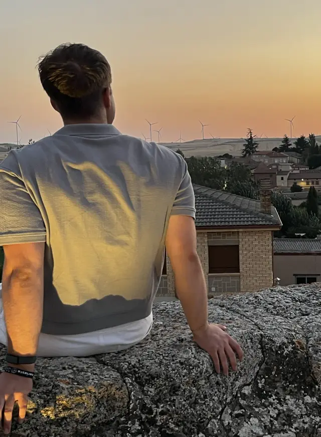 Sitting on a stone wall at dusk, looking out over Los Balbases (Burgos) with its church on the hill and wind turbines along the horizon.