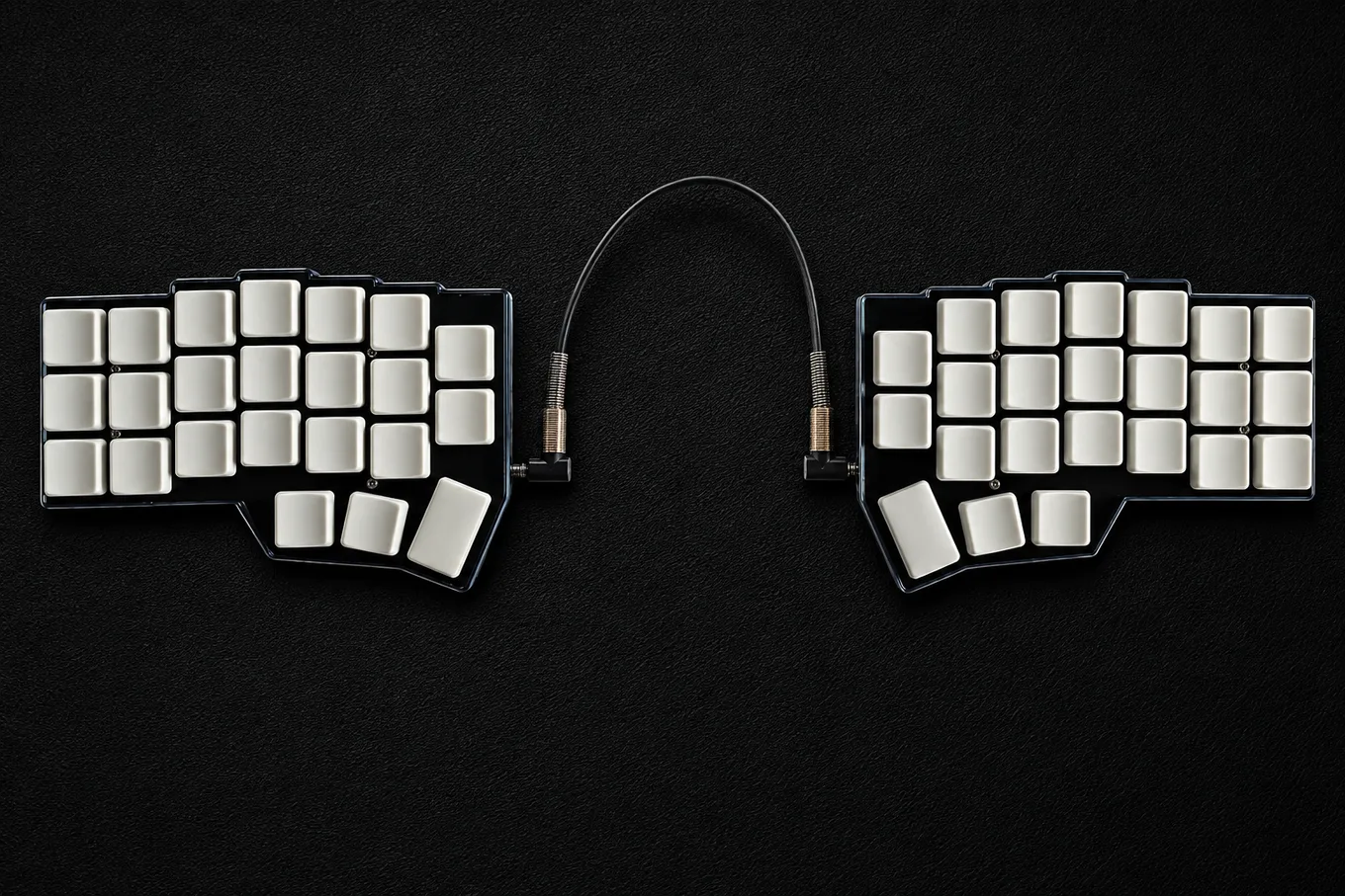 Top view of a wired Corne V4 split keyboard with two black low-profile halves, 42 blank white keycaps and a central TRRS cable.