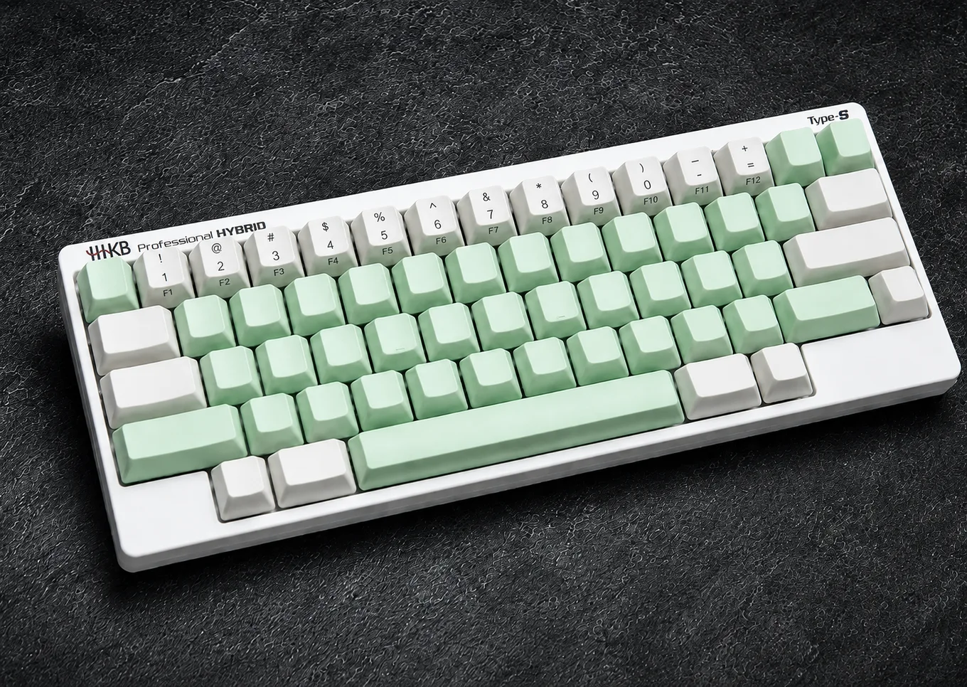 Three-quarter view of the assembled white HHKB Professional Hybrid Type-S with mint and white keycaps on a dark textured surface.